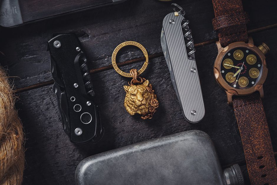 Close-up of lifestyle accessories including Swiss army knife, watch, and tiger key ring on a dark surface.