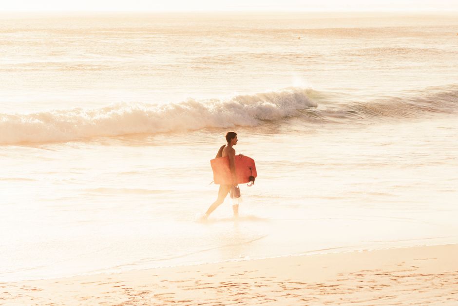 A surfer with a board enjoys a serene sunset at Arraial do Cabo beach, Brazil.