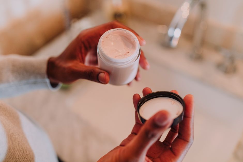Hands holding an open jar of face moisturiser