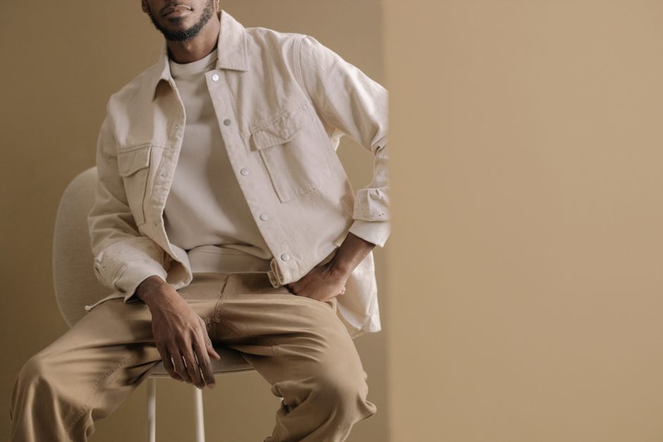 Minimalistic portrait of a man wearing a beige jacket and pants, sitting casually indoors with neutral tones.