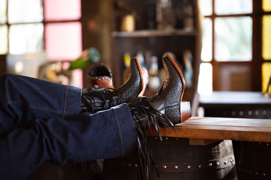 Close-up of relaxed legs in cowboy boots on a barrel in a rustic indoor setting.
