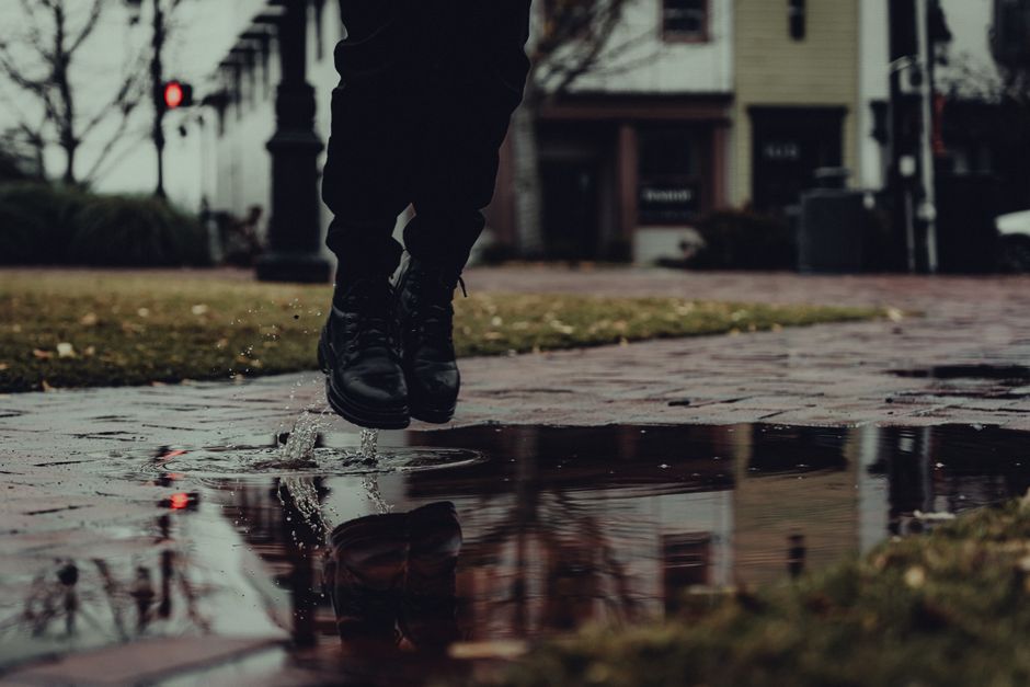 Captured motion of boots jumping over a puddle on a rainy day in an urban park setting.