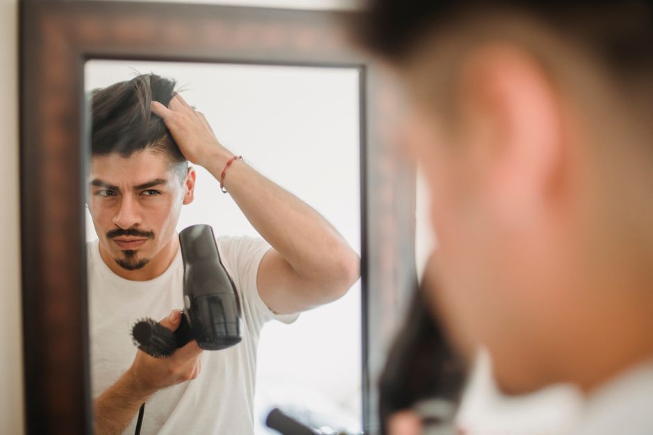 Man drying and shaping his hair in a bathroom mirror
