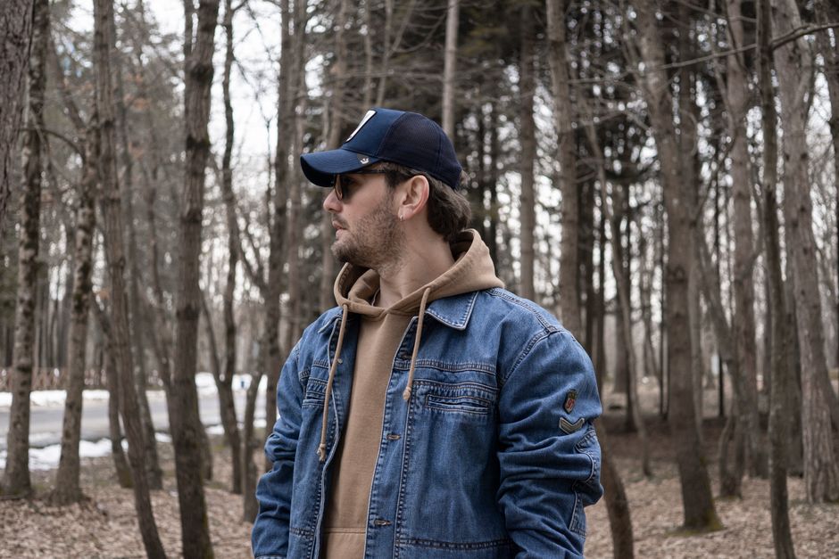 Man in a denim jacket and cap standing among trees