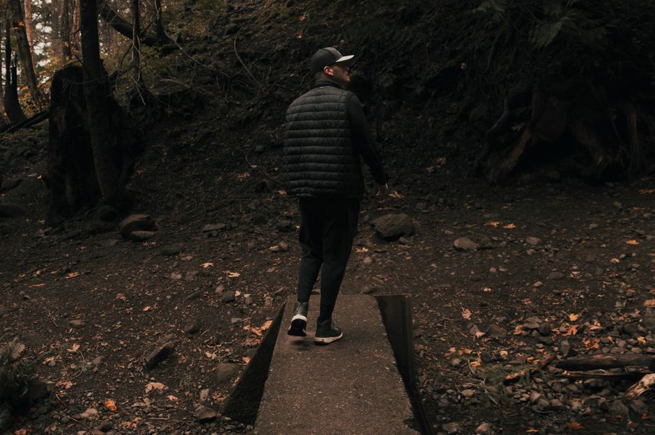 Man wearing a puffer jacket walks through a forest trail, surrounded by autumn leaves.