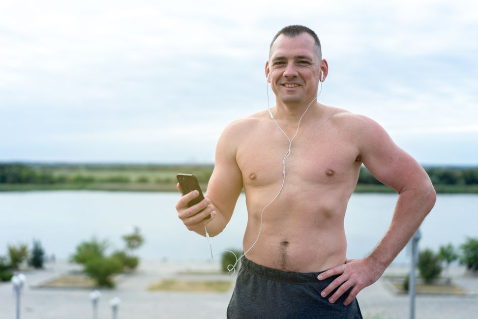 Muscular man outdoors, listening to music while exercising, smiling.