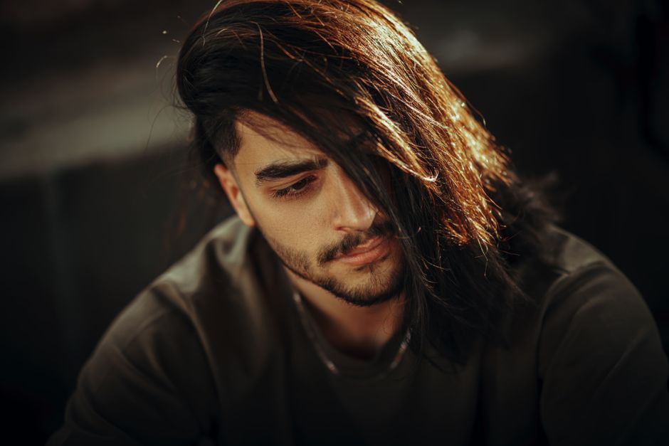 A contemplative man with long dark hair in soft, warm lighting.
