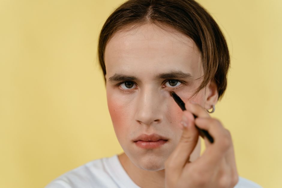 Detailed close-up of a man applying makeup with a brush in a studio setting against a yellow background.