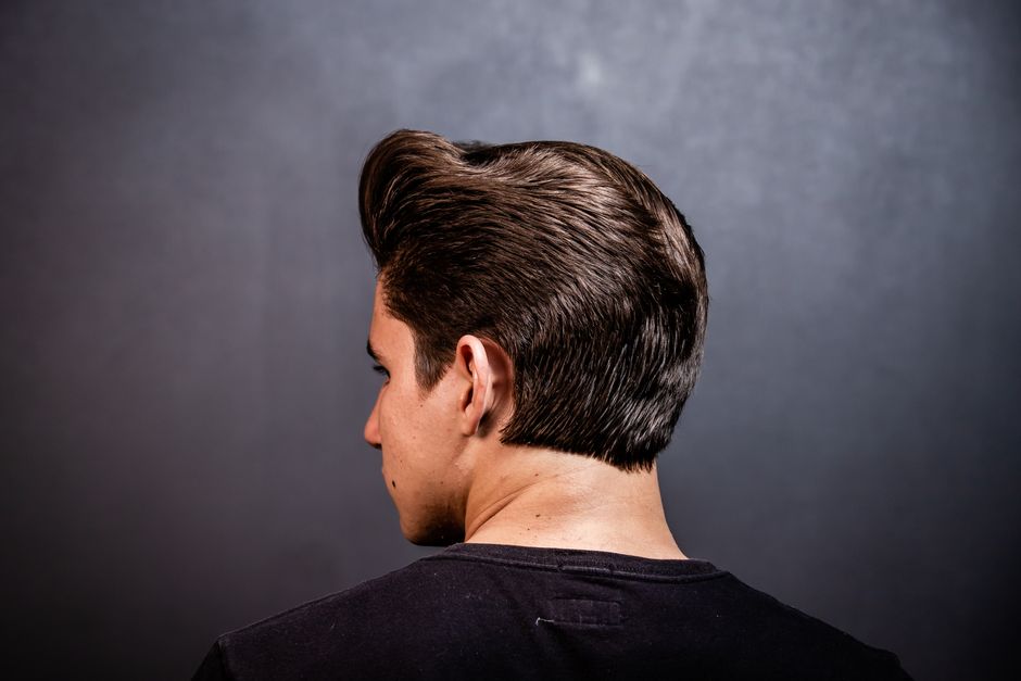 Close-up of a man's stylish hairstyle from the back against a grey background.