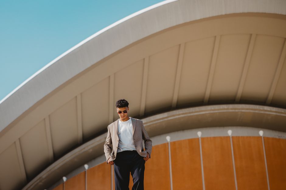 Man in stylish attire standing in front of Berlin's iconic architecture on a sunny day.