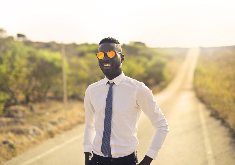 Cheerful black formal dressed man in funny sunglasses toothy smiling while standing on road in countryside