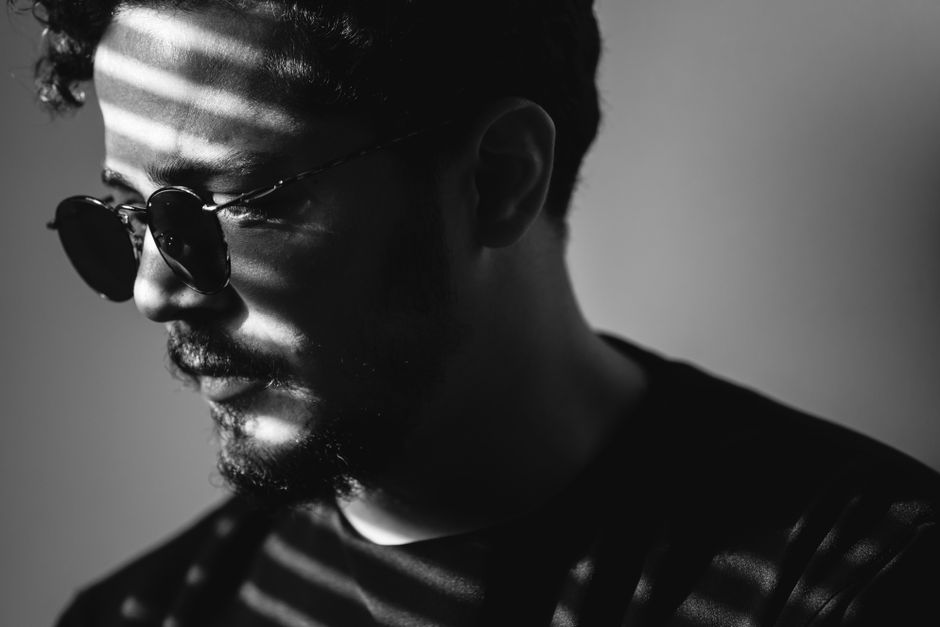 Black and white portrait of a man wearing round sunglasses with dramatic lighting and shadows.
