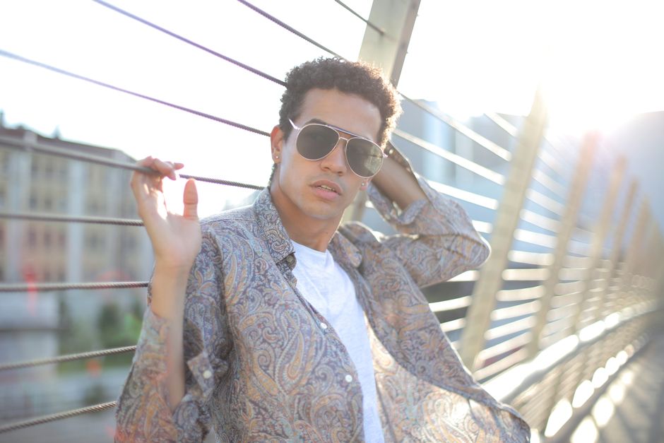 Trendy man poses on a city bridge, embracing sunlight and fashion.
