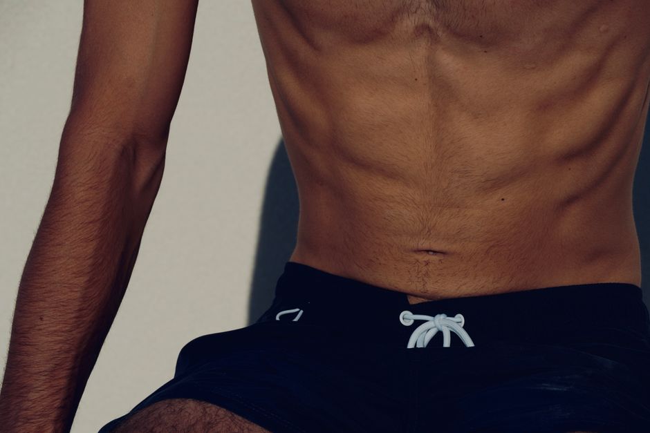 Close-up image of a fit shirtless man wearing black shorts, highlighting a toned physique.