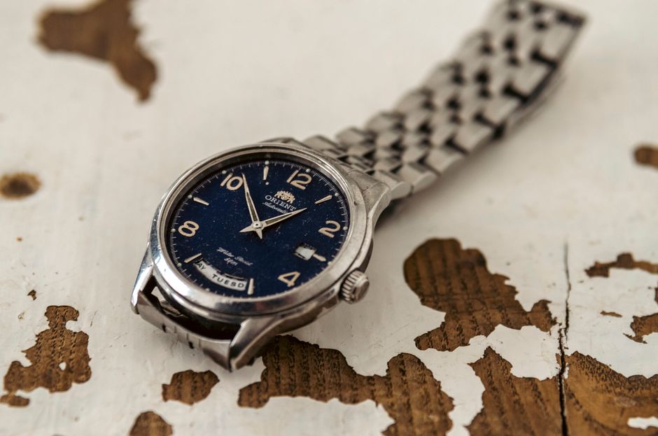 Close-up of a vintage Oriental wristwatch with a metal strap on a distressed wooden surface.