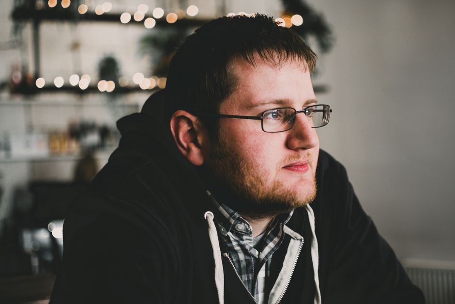 Portrait of a thoughtful man in glasses, indoors with warm bokeh lighting.