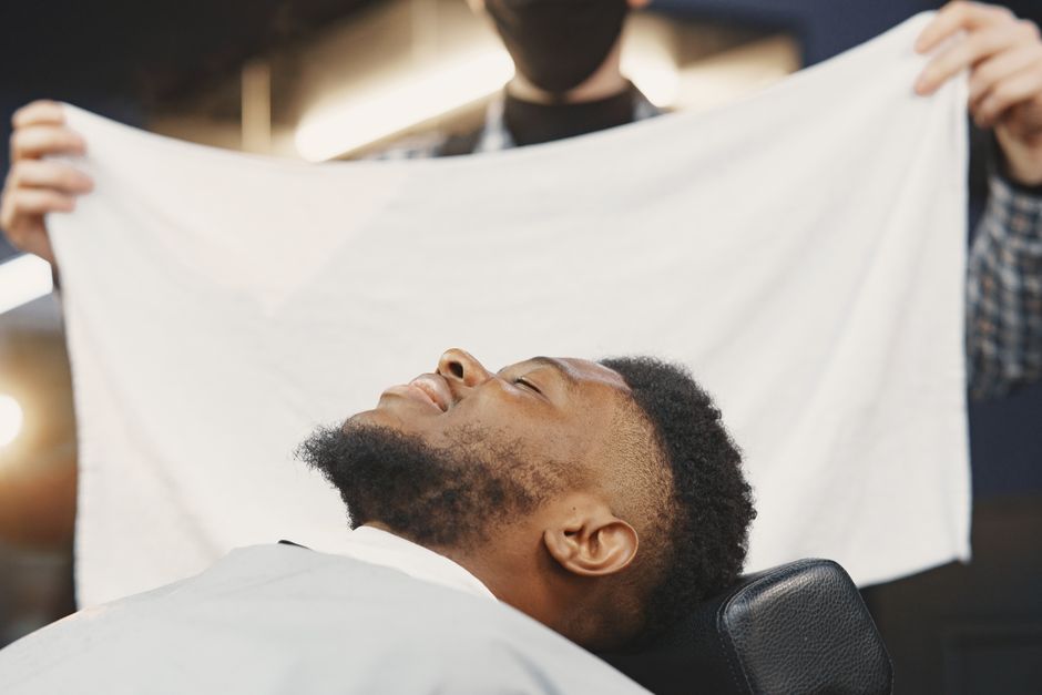 Black man enjoying a hot towel treatment at a barbershop for a pampering experience.
